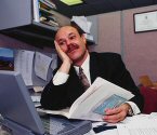 photo of a man in an office cubicle sitting in front of his computer wtih a bored look